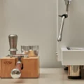 IKAPE Buchenstation mit silbernem Tamper, Distributor und Siebträger neben einer Espressomaschine