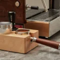 Tamperstation aus Buche auf Marmor mit schwarzem Tamper, silbernem Distributor und gefülltem Siebträger