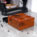 Leere Tamperstation auf grauem Stein mit Kaffeebohnen ringsum, daneben der breite Ring, dahinter eine Hebelmaschine