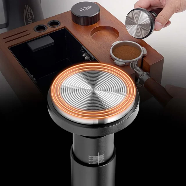 Tamper mit der Basis nach oben, die Fläche mit Ringen orange umrandet, vor einer Organizer-Box aus Holz und einem Siebträger