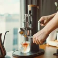 Hand dreht die Kurbel der Alkaid, während Espresso in ein Glas mit Eis auf dem Sockel läuft