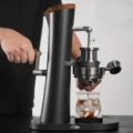 Person dreht hinter der Alkaid die Kurbel, Espresso tropft in ein Glas mit Eis auf einer kleinen Unterlage