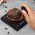 Hand sprüht mit der schwarzen Flasche über die Kaffeebohnen in der Schale auf der Waage