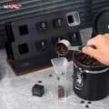 Hand löffelt Bohnen aus einer Dose in ein klares Röhrchen mit eckigem Trichter obenauf, dahinter der Ständer