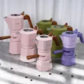 Rosa, grüne und violette Espressokocher in verschiedenen Höhen auf grauem Marmor vor einem weißen Vorhang