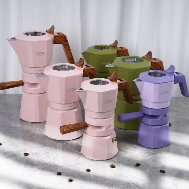 Rosa, grüne und violette Espressokocher in verschiedenen Höhen auf grauem Marmor vor einem weißen Vorhang