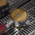 Goldenes Clockwork-Sieb in einem Bottomless-Siebträger mit gestreiftem Griff auf einer Abtropfschale aus Stahl