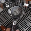 Hand hält einen Siebträger mit eingesetztem silbernem Clockwork-Sieb über die Abtropfschale einer Maschine