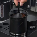 Nahaufnahme: Finger drehen den Hebel im Becher, darin Kaffeemehl, daneben ein Distributor