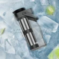 Schwarzer Cold-Brew-Krug liegend in Eis mit Limettenspalten, der Siebfilter durch das Glas sichtbar