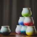 Sieben Verlaufstassen als kleine Pyramide vor einem dunklen Vorhang, links abseits eine dunkle Tasse
