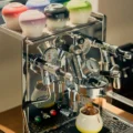Verlaufstassen umgedreht oben auf einer Espressomaschine, auf der Abtropfschale fängt eine gelbe Tasse Espresso auf Eis auf