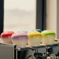 Rote, rosa, gelbe und hellgrüne Tasse umgedreht in einer Reihe auf einer Espressomaschine am Fenster