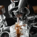 Espresso läuft aus einem Bottomless-Siebträger in ein Glas mit Eis unter einer verchromten Espressomaschine
