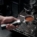 Hand hält den Siebträger mit getamptem Kaffeebett mit Ringmuster über die Tropfschale einer Espressomaschine