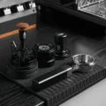 CUBOID Siebträger auf einer schwarzen Barmatte vor einem Nadelverteiler, einem Distributor und einem Tamper