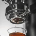 Unterseite des bodenlosen Siebs in der Brühgruppe, Espresso tropft in ein kleines Glas