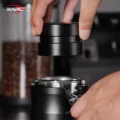 Hand hebt den Distributor gerade vom Siebträger ab, dahinter unscharf Gläser mit Kaffeebohnen