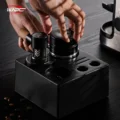 Hände stellen den Distributor in eine schwarze Werkzeugstation neben einen Tamper, Kaffeebohnen auf dem dunklen Tisch