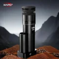 Schwarze IKAPE Mühle auf einem Haufen Kaffeemehl und Bohnen vor einer nächtlichen Berglandschaft