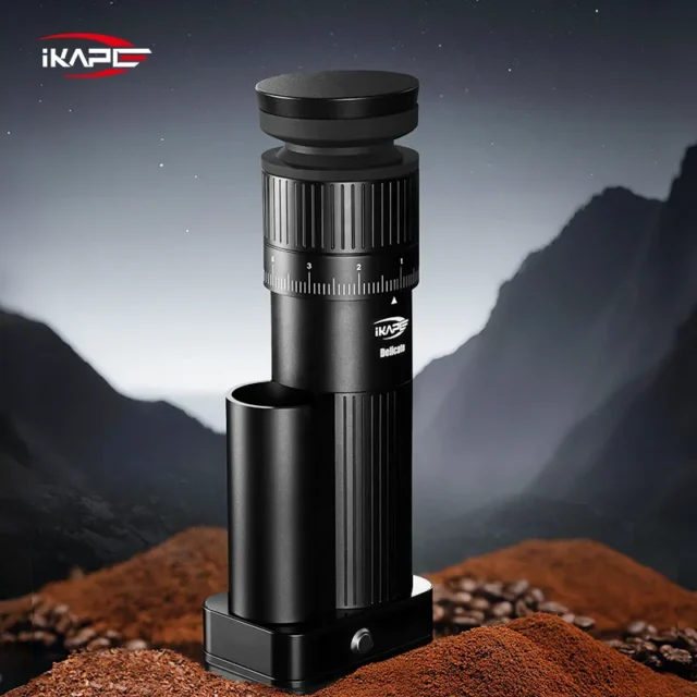 Schwarze IKAPE Mühle auf einem Haufen Kaffeemehl und Bohnen vor einer nächtlichen Berglandschaft