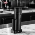 Schwarze IKAPE Mühle auf einer weißen Marmorplatte, dahinter unscharf eine Kaffeebar