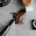 Draufsicht auf verschüttetes Kaffeemehl auf einer Marmorfläche, die Düse des schwarzen IKAPE Saugers am Rand