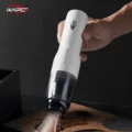 IKAPE Kaffee Staubsauger in Weiß, in einer Hand, saugt verschüttetes Kaffeemehl von einem Holztablett