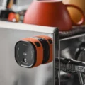 Orange Sprühflasche an der Stahlseite einer Espressomaschine aufbewahrt, oben im Regal Becher
