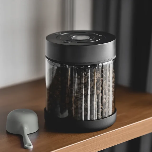 IKAPE Vakuumdose Kaffee, mit Kaffeebohnen gefüllt, auf einem Holzregal, daneben ein grauer Löffel