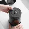Finger drückt eine Taste am Deckel der Dose, in der Mitte leuchtet das kleine runde Display