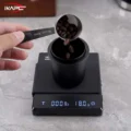 Kaffeebohnen fallen aus einem Löffel in den schwarzen Dosierbecher auf einer Waage, die 18,0 g anzeigt