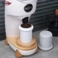 Weißer Dosierbecher unter dem Auswurf einer weißen Mühle mit Holzfüßen fängt Kaffeemehl auf, daneben ein zweiter Becher