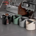 Schwarzer Abklopfbehälter mit Siebträger auf der Stange, daneben grüner, grauer und cremefarbener an einer Espressomaschine
