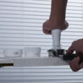 Hand tampt mit dem weißen Tamper in einen Siebträger am Rand der weißen Matte, dahinter Trichter und Distributor