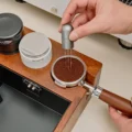 Hand rührt mit einem grauen WDT-Tool im Kaffeemehl eines Siebträgers, der im Organizer steckt