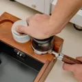 Hand drückt einen dunklen Tamper in einen Siebträger im Organizer, daneben ein weißer Distributor