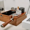 Set mit Siebträger im seitlichen Schlitz auf weißer Arbeitsfläche, zwischen einer Mühle und einer Espressomaschine