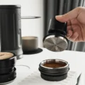 Hand hebt den Geometry Impact-Tamper gerade von einem Sieb mit getamptem Kaffee auf einer weißen gerippten Matte