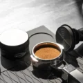 Schwarzer Distributor neben einem Siebträger mit getamptem Puck mit Ringmuster, dahinter ein Tamper mit Ringen an der Basis