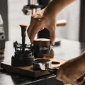 Hand senkt den Schwerkraft-Distributor am Holzkopf auf einen Siebträger mit Kaffeemehl auf einem Holzbrett