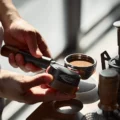 Hand hält den Distributor neben einem Siebträger, dessen Kaffee flach geebnet ist
