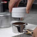 Hand senkt den weißen Distributor auf einen Siebträger mit Kaffeemehl, links unscharf ein silberner Distributor