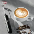 Aufschäumer mit Spiralquirl auf grauem Marmor neben einem Latte mit Herz im Schaum und Kaffeebohnen