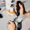 Zwei Hände bei der Arbeit, eine hält den Aufschäumer aufrecht, die andere ein Stahlkännchen mit Milch