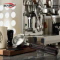 IKAPE Hantom Bottomless-Siebträger auf einem Holzbrett vor einer verchromten Espressomaschine