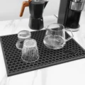 Zwei umgedrehte Gläser und eine Glaskanne tropfen auf der Matte ab, dahinter ein Espressokocher und eine Kaffeemaschine