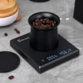 V2 Becher voller ganzer Kaffeebohnen auf einer schwarzen Digitalwaage, daneben liegt sein Deckel