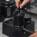 Hand hebt den Mittelhebel des V2 Bechers, der auf einem Siebträger in einem schwarzen Ständer sitzt