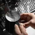 Dampflanze lässt die Milch im schwarzen Kännchen rollen, die ml-Skala an der polierten Innenwand sichtbar